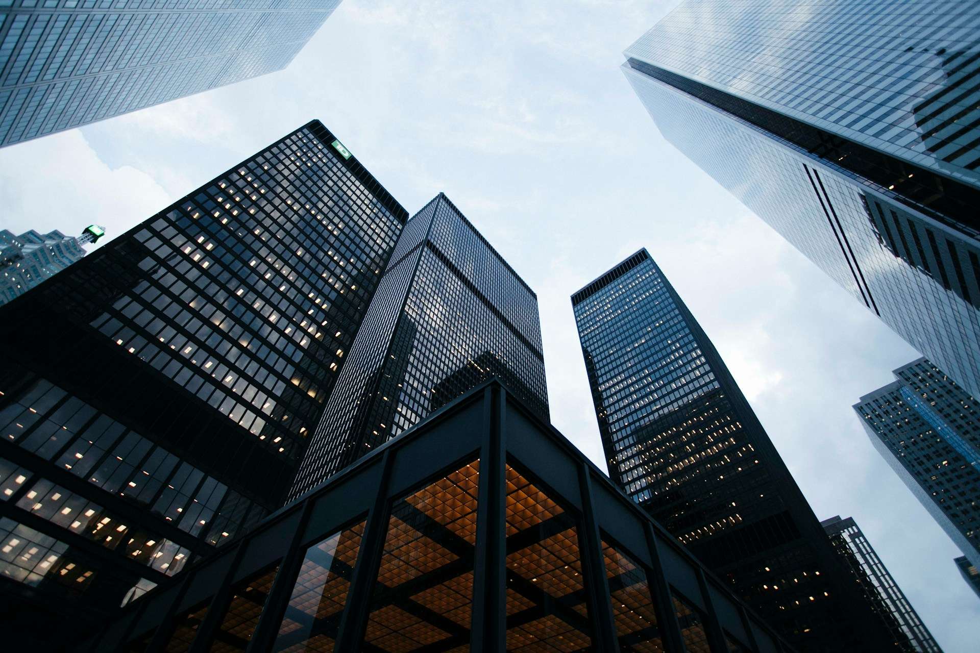 Looking up at several tall modern office skyscrapers with glass windows against a cloudy sky.